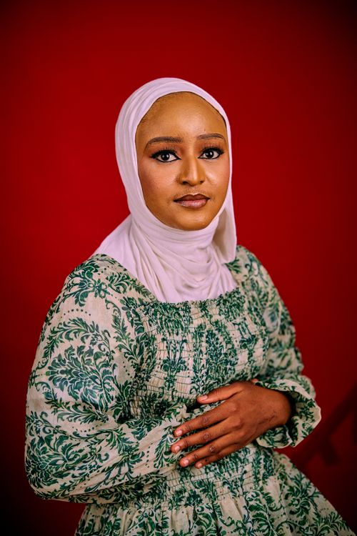 Free Elegant portrait of a woman wearing a hijab and a patterned dress against a red background. Stock Photo