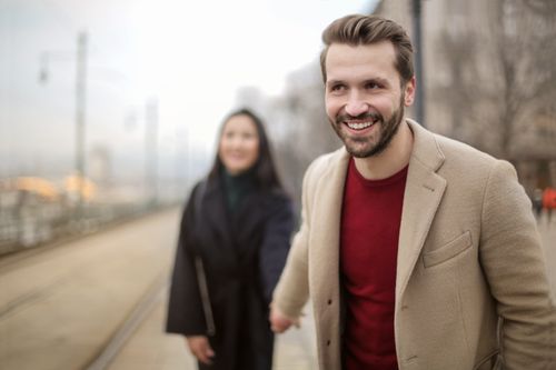Free Happy young couple holding hands and smiling on a city street, wearing stylish coats on a daytime walk. Stock Photo