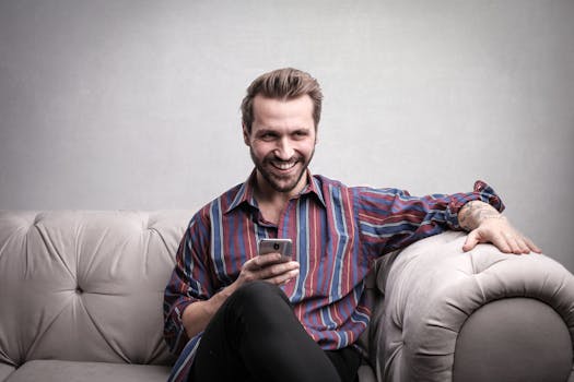 A cheerful man sitting comfortably on a sofa using his smartphone indoors.