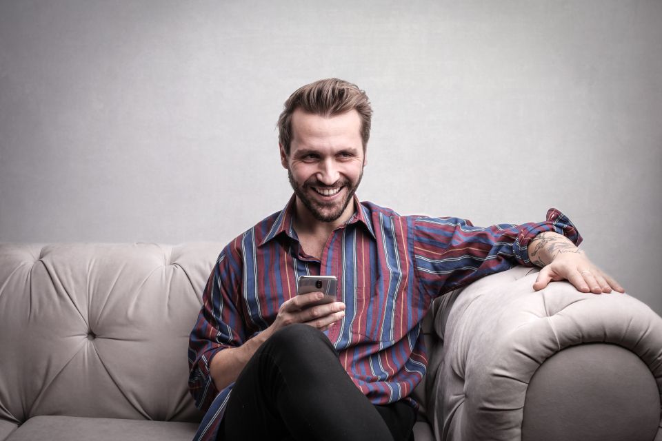 A cheerful man sitting on a sofa using his smartphone