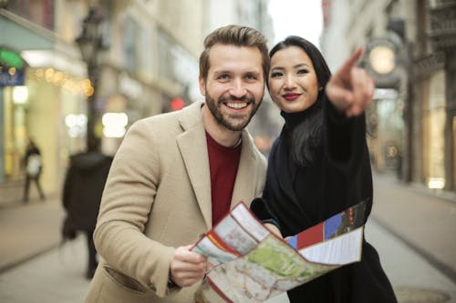 Man in Brown Suit Holding a Map Smiling Beside Woman in Black Coat