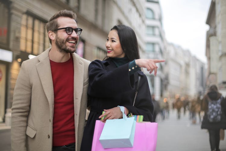 Joyful Multiethnic Adult Couple With Shopping Bags Walking Along Street In Downtown