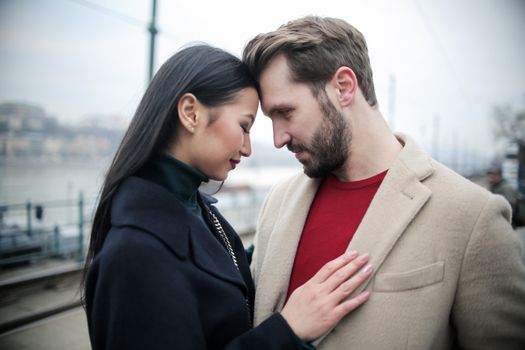 Happy multiracial couple hugging on waterfront while having romantic date in city