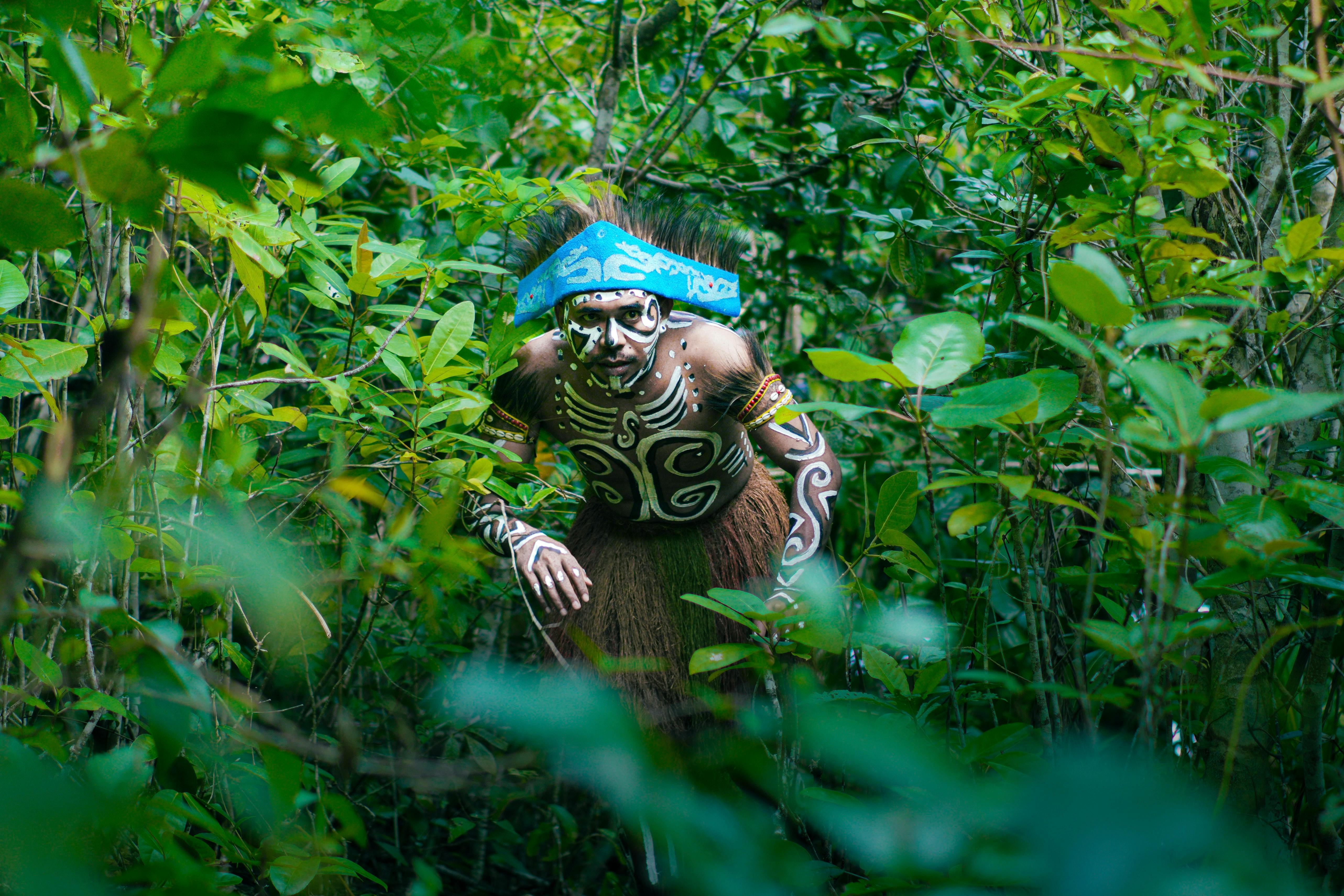 Man in traditional tribal costume performing dance amidst the vibrant Papuan forest.