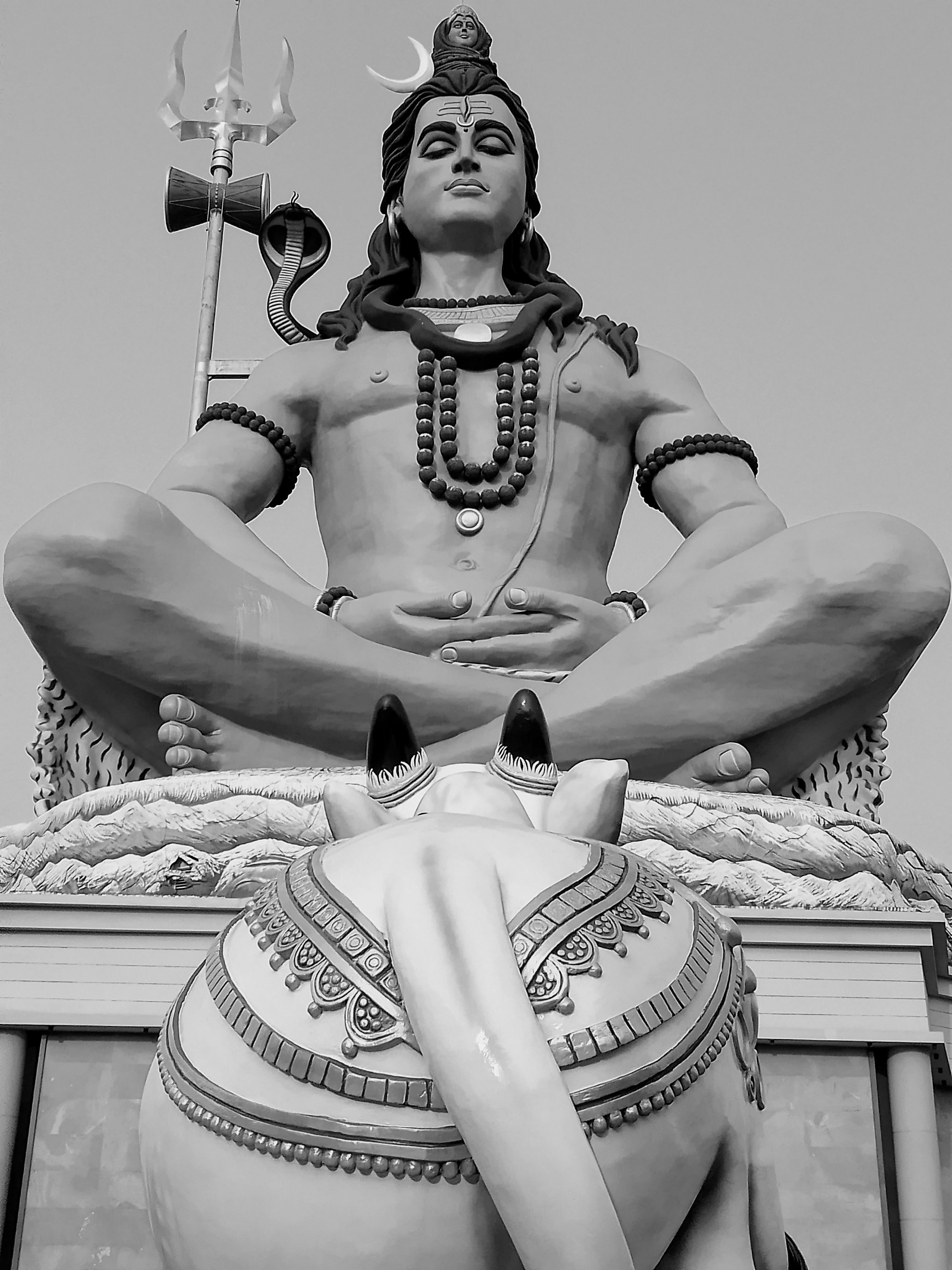 A striking black and white photo of a large Lord Shiva statue with Nandi in the foreground.
