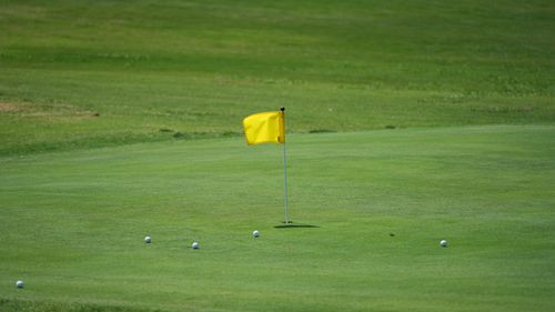 Free Golf course scene with yellow flag and golf balls on green under a clear sky. Stock Photo