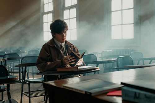 Free A young man engrossed in a book in a sunlit, atmospheric classroom setting. Stock Photo