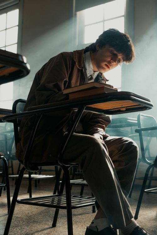 Free Contemplative student sitting in a classroom with sunlight streaming through windows. Stock Photo
