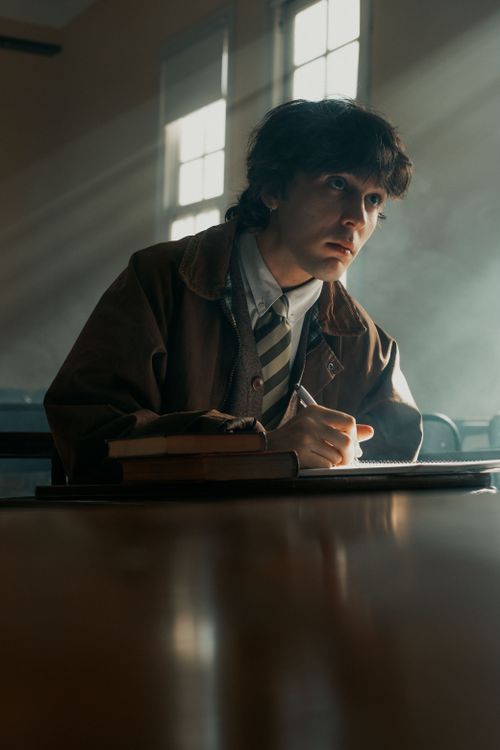 Free A contemplative student sits in a sunlight classroom with a stack of books, absorbed in thought. Stock Photo