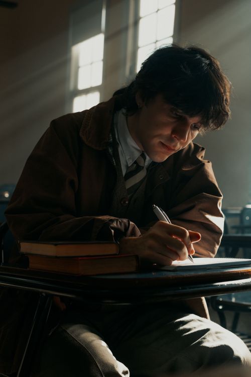 Free A focused student studying in a classroom, illuminated by natural light through windows. Stock Photo