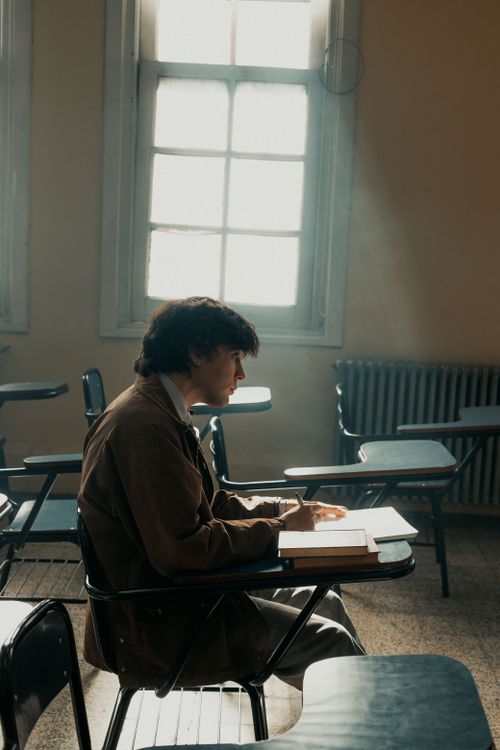 Free A student sits alone in a sunlit classroom, deep in thought, contemplating study materials. Stock Photo