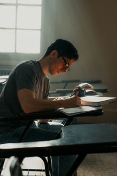 A student concentrating on studies in a classroom with sunlight streaming in through a window.