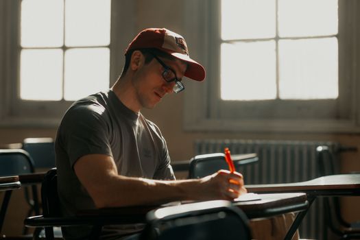A student in a sunlit classroom concentrating on notes with a pen.