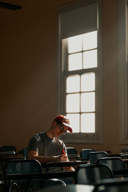 A student wearing a cap studies diligently in a sunlit classroom. A student wearing a cap studies diligently in a sunlit classroom.