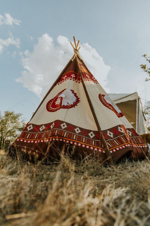 Free A beautifully decorated teepee tent set outdoors under a clear sky, showcasing traditional patterns and vibrant colors. Stock Photo