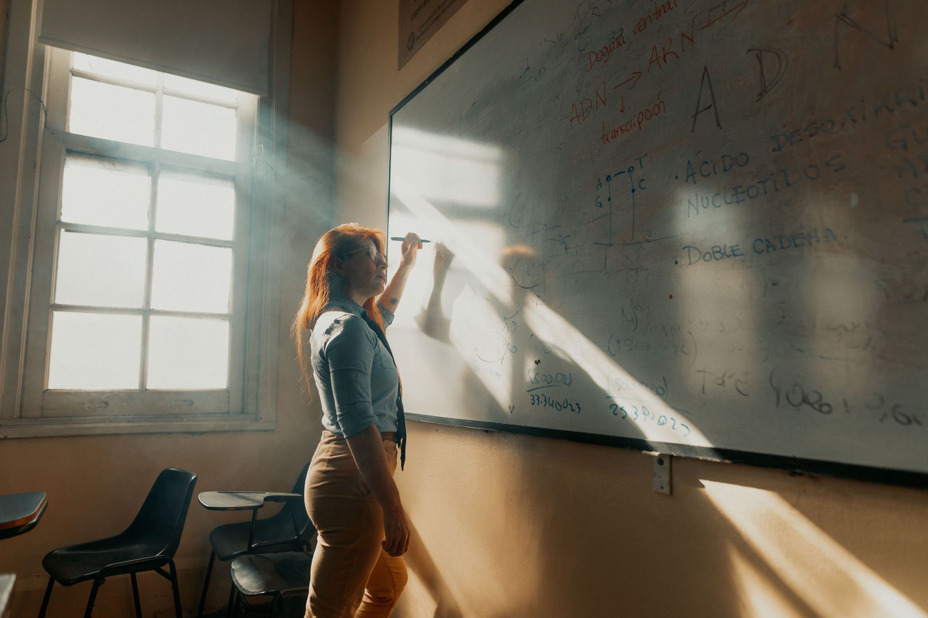 A teacher in Buenos Aires writes on a whiteboard in natural light streaming through a window.