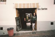 Streetfront view of Dos Barrios cafe with a woman at the entrance in Quito, Ecuador.