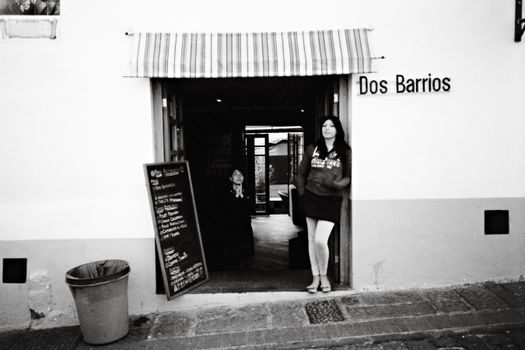 Black and white photo capturing entrance of Dos Barrios restaurant in Quito with woman standing at doorway.