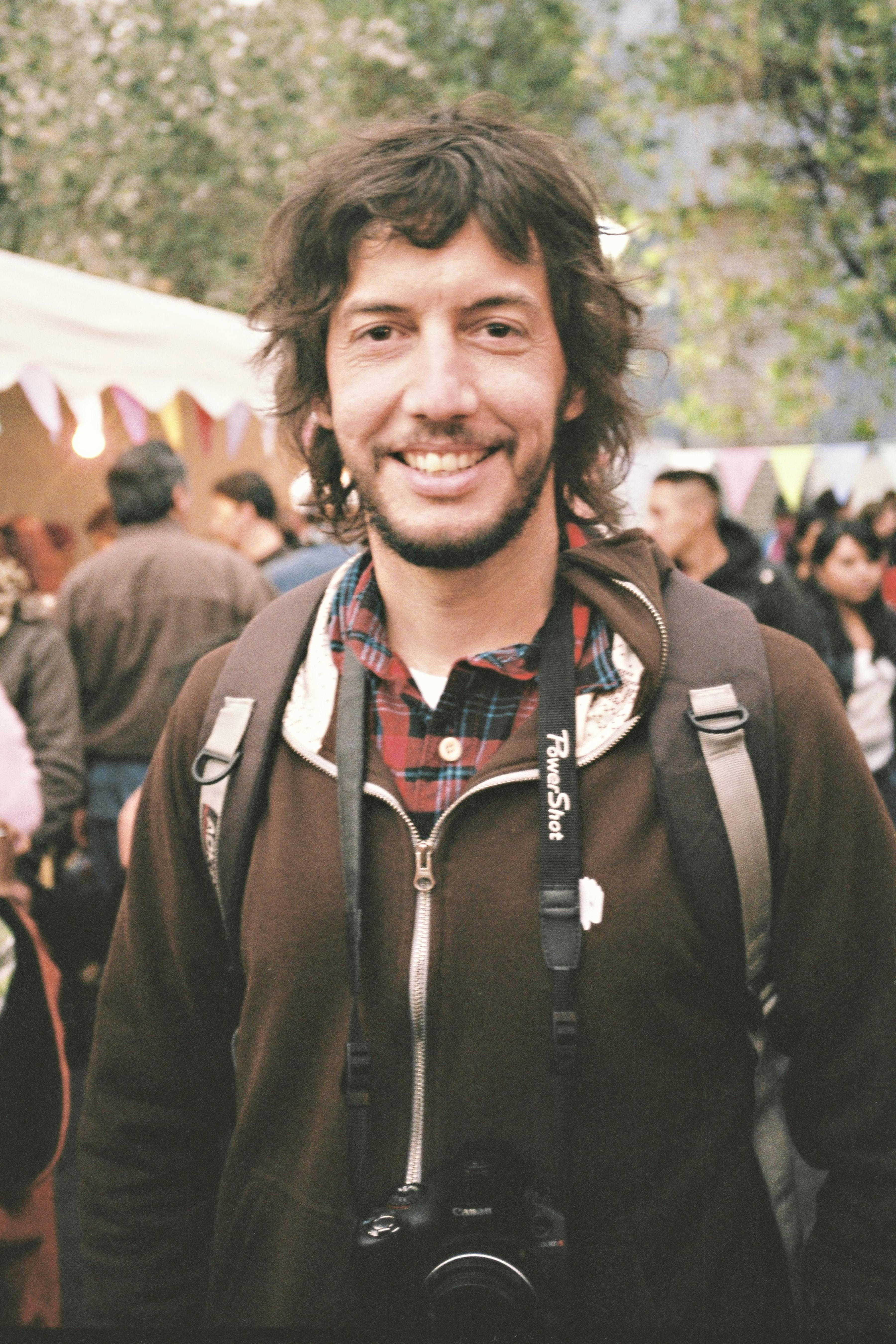 Portrait of a smiling man with a backpack and camera at an outdoor festival in Quito, Ecuador.