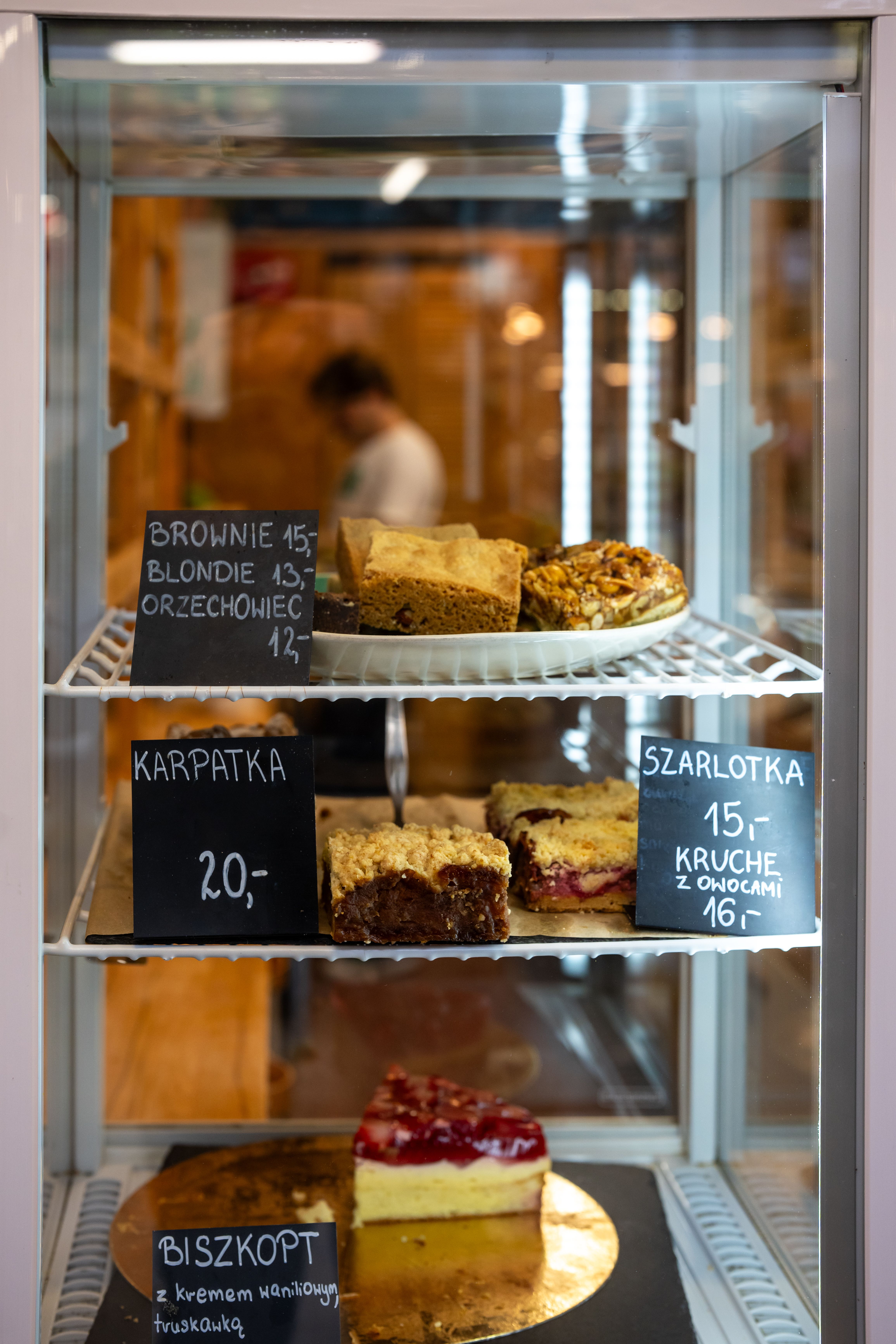 Close-up of Polish pastries with price tags in a bakery fridge display.