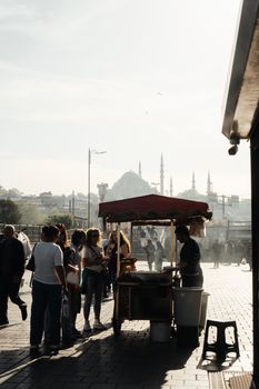 A street vendor serves customers near a recognizable mosque in Istanbul at dusk.