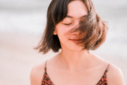 Free Charming Asian woman with short brown hair closing eyes and waving with hair in wind Stock Photo