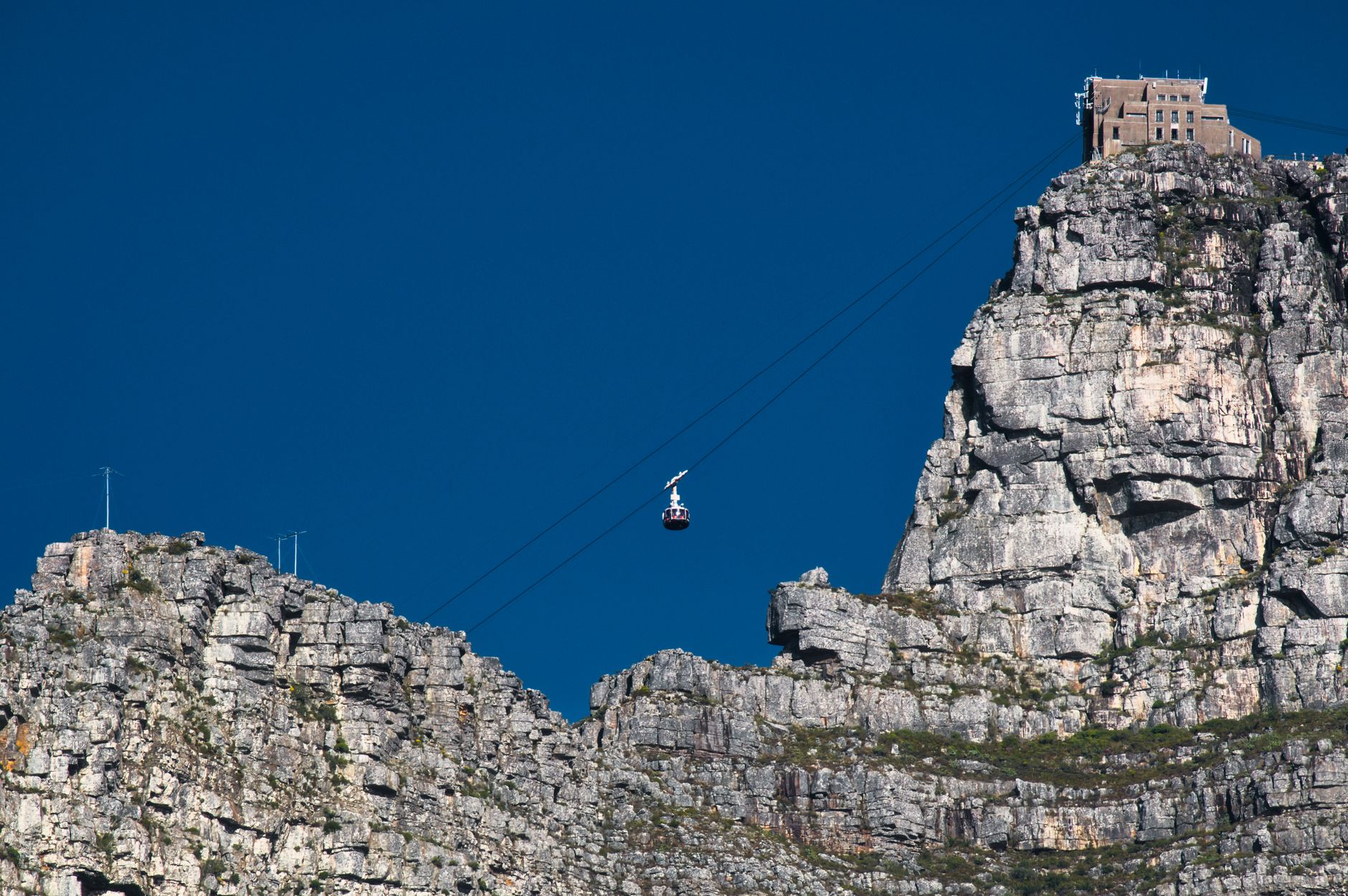 A cable car of the Table Mountain aerial cableway climbing the cliffs against a clear blue sky, Cape Town
