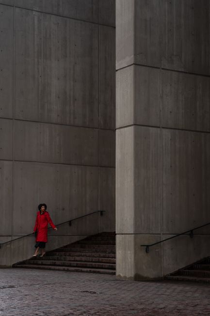 Dramatic shot of a woman in a red coat standing against a modern architectural concrete wall.