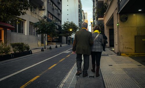 Free Senior couple walking arm in arm down a city street at dusk, showcasing companionship and urban life. Stock Photo
