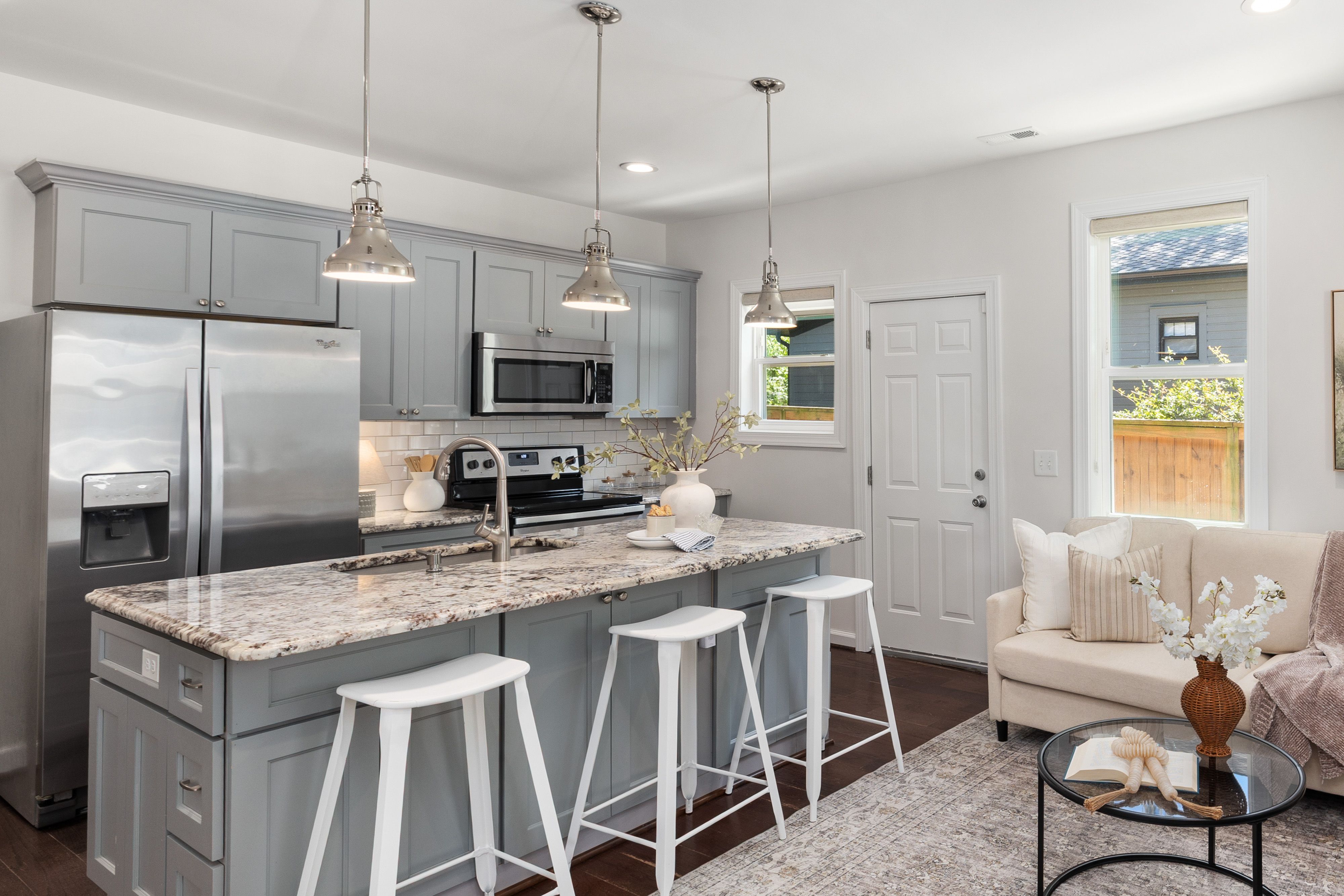 Bright grey kitchen with a granite island, pendant lights and stainless steel appliances