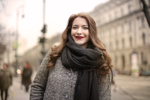 一位穿着灰色外套、围着围巾的幸福女人站在城市街道上，在户外展露着迷人的微笑