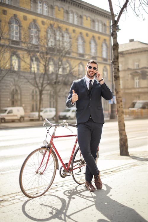 Man in Black Suit Standing Beside Red Bicycle