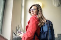 一位戴着眼镜、穿着红色外套的女士在室内微笑着手拿书本