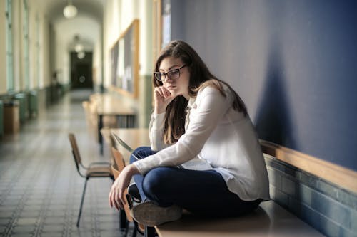 Wanita Dengan Kemeja Lengan Panjang Putih Dan Jeans Denim Biru Duduk Di Atas Meja