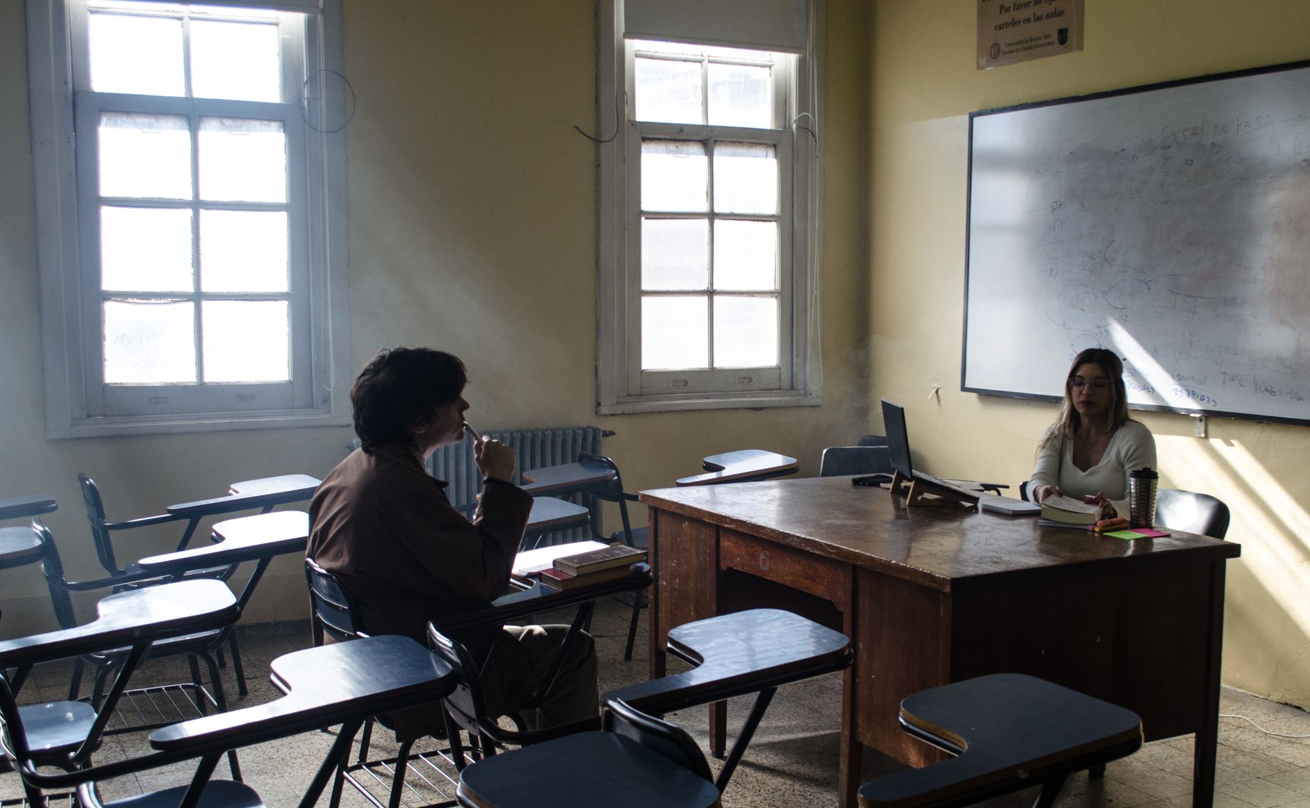 Two students conversing in a classroom at a Buenos Aires university. Bright, educational setting.