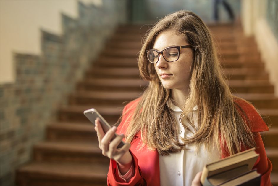 Portrait of a young woman in glasses checking her smartphone inside a building.