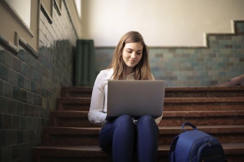 Free Young woman sitting on stairs using laptop for remote work. Perfect for promoting digital nomad lifestyle. Stock Photo
