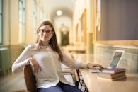 一位戴着眼镜、身穿白色上衣的年轻女子，正在研究区域使用笔记本电脑，面带微笑