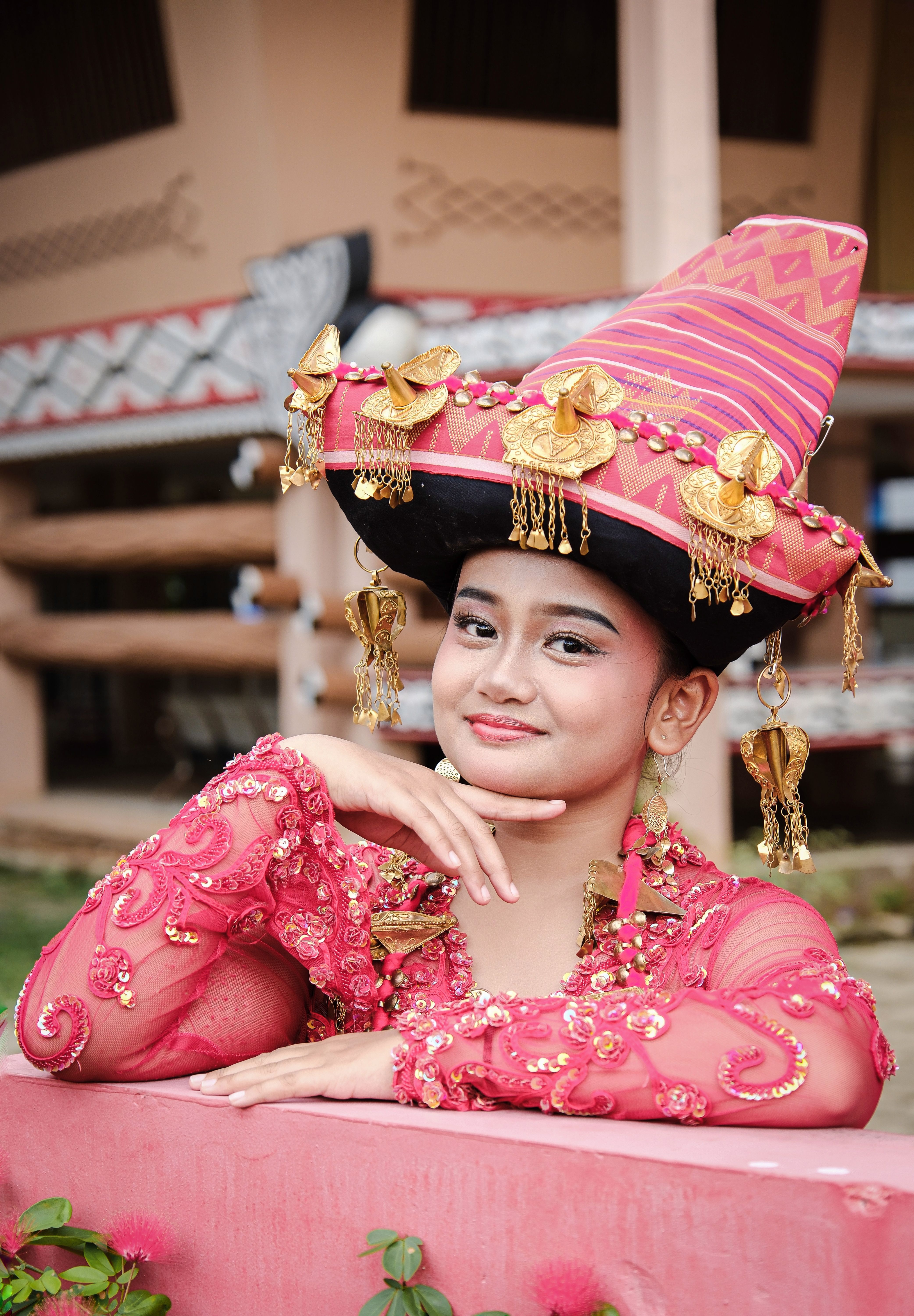 Young woman in vibrant traditional Minangkabau dress and hat, smiling outdoors in Indonesia.