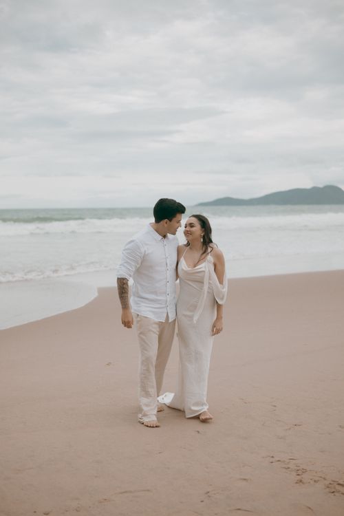 Free A couple in white clothing enjoying a romantic walk along a serene tropical beach. Stock Photo
