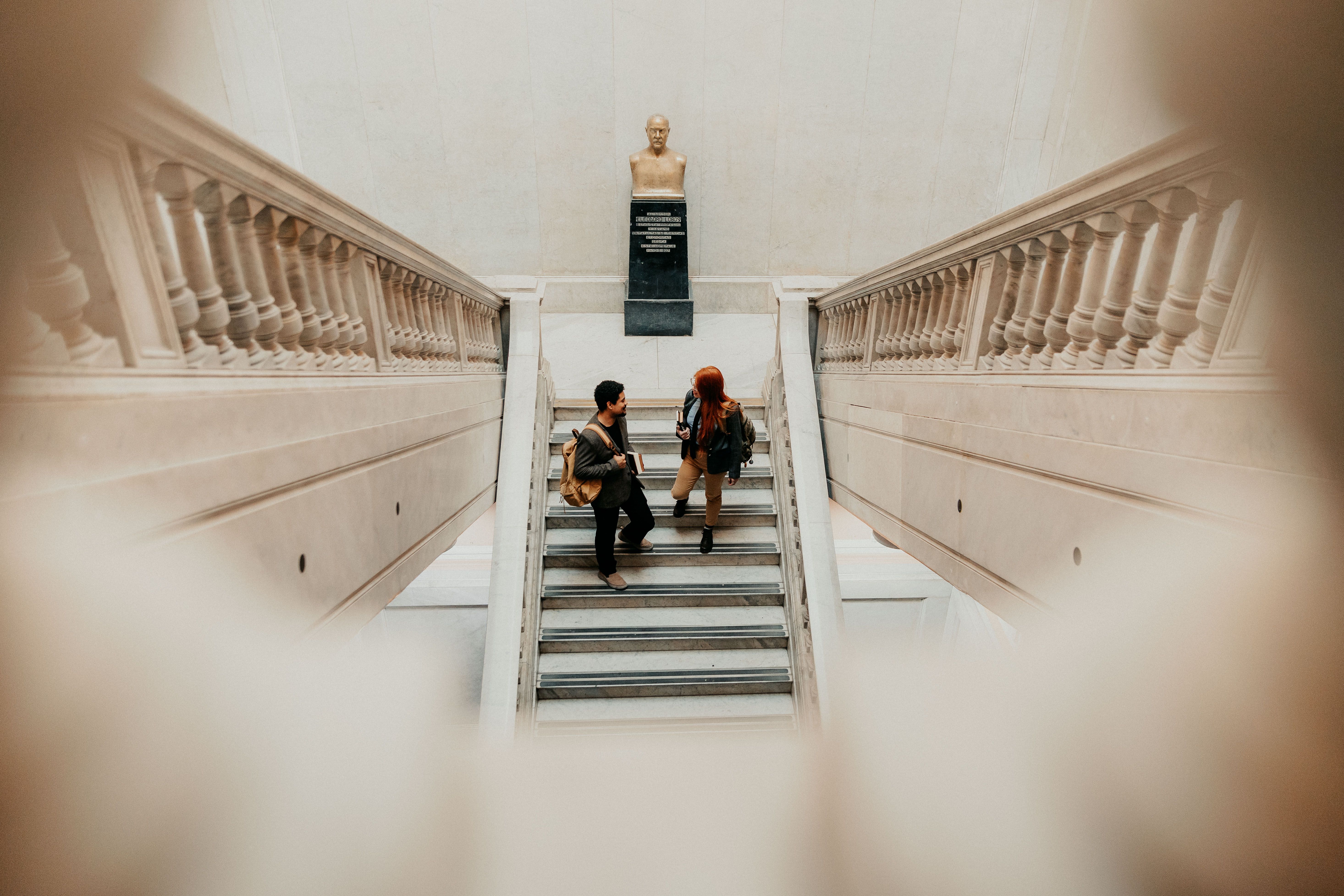 Dos estudiantes conversando en una gran escalinata con un busto en la universidad de Buenos Aires.