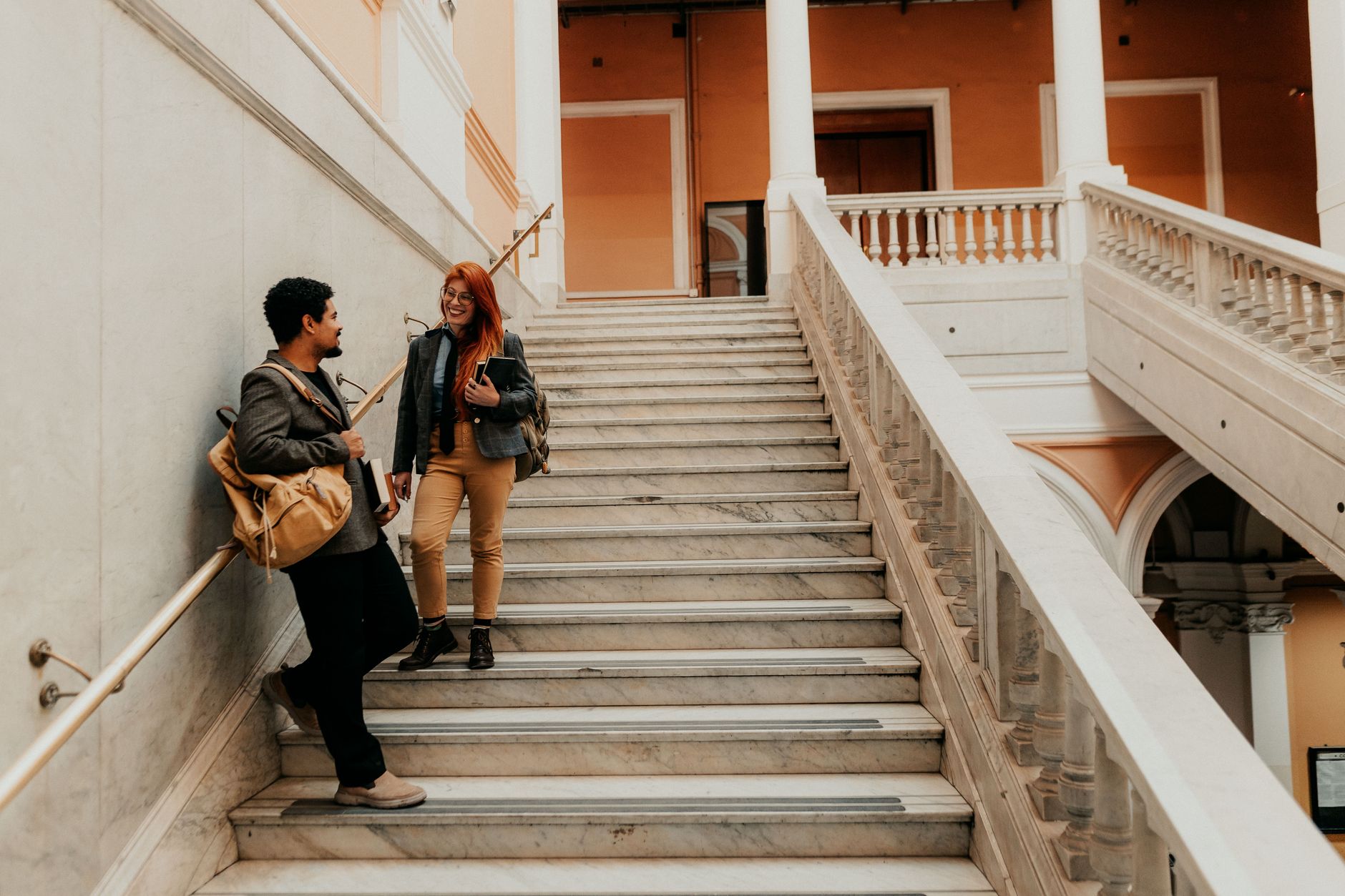Two university students chatting on elegant marble stairs in architectural building.