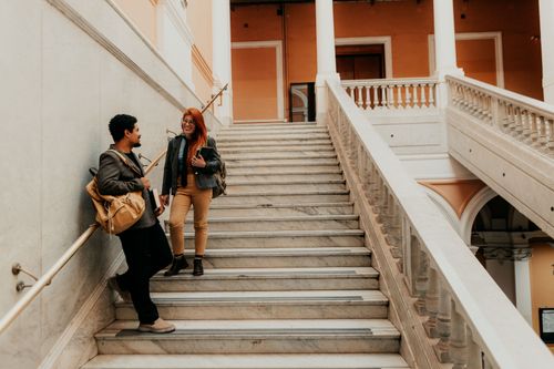 Free Two university students chatting on elegant marble stairs in architectural building. Stock Photo