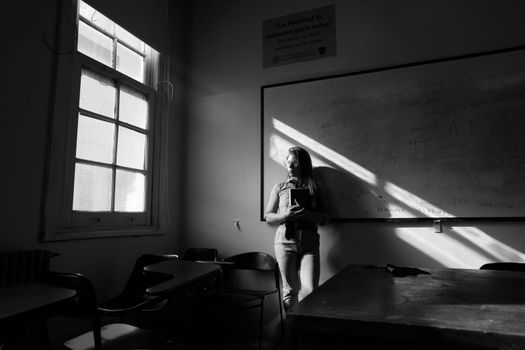 A thoughtful student stands in a sunlit classroom in Buenos Aires, evoking a sense of contemplation.