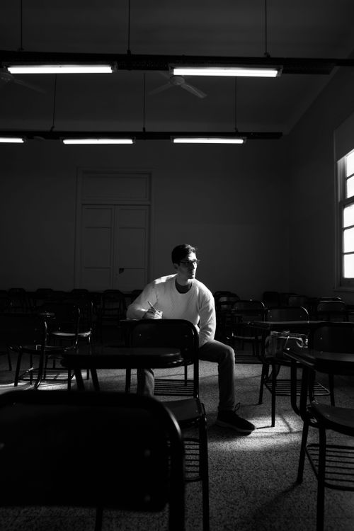 Free A lone student in a dimly lit classroom, bathed in natural light from a window. Stock Photo