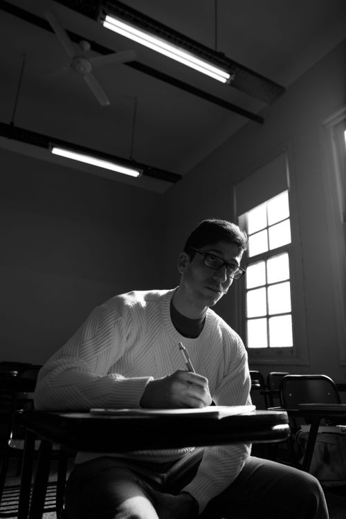Free Black and white photo of a young male student writing in a classroom setting. Stock Photo