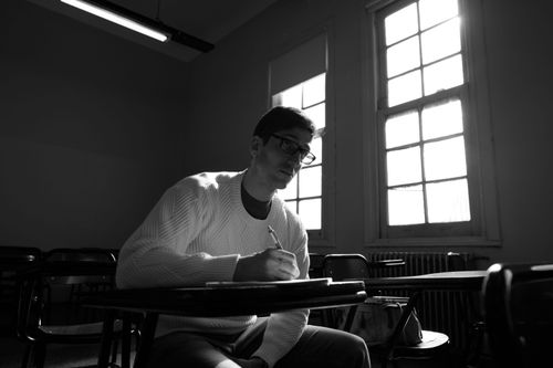 Free Student writing notes in a vintage classroom with sunlight streaming through the windows. Stock Photo