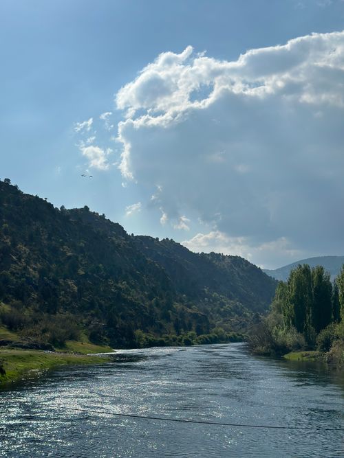 Free Tranquil river flows through a scenic valley with lush green hills and cumulus clouds. Stock Photo