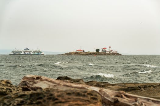 Picturesque view of a ferry crossing near a lighthouse on a rocky island in Victoria, BC.