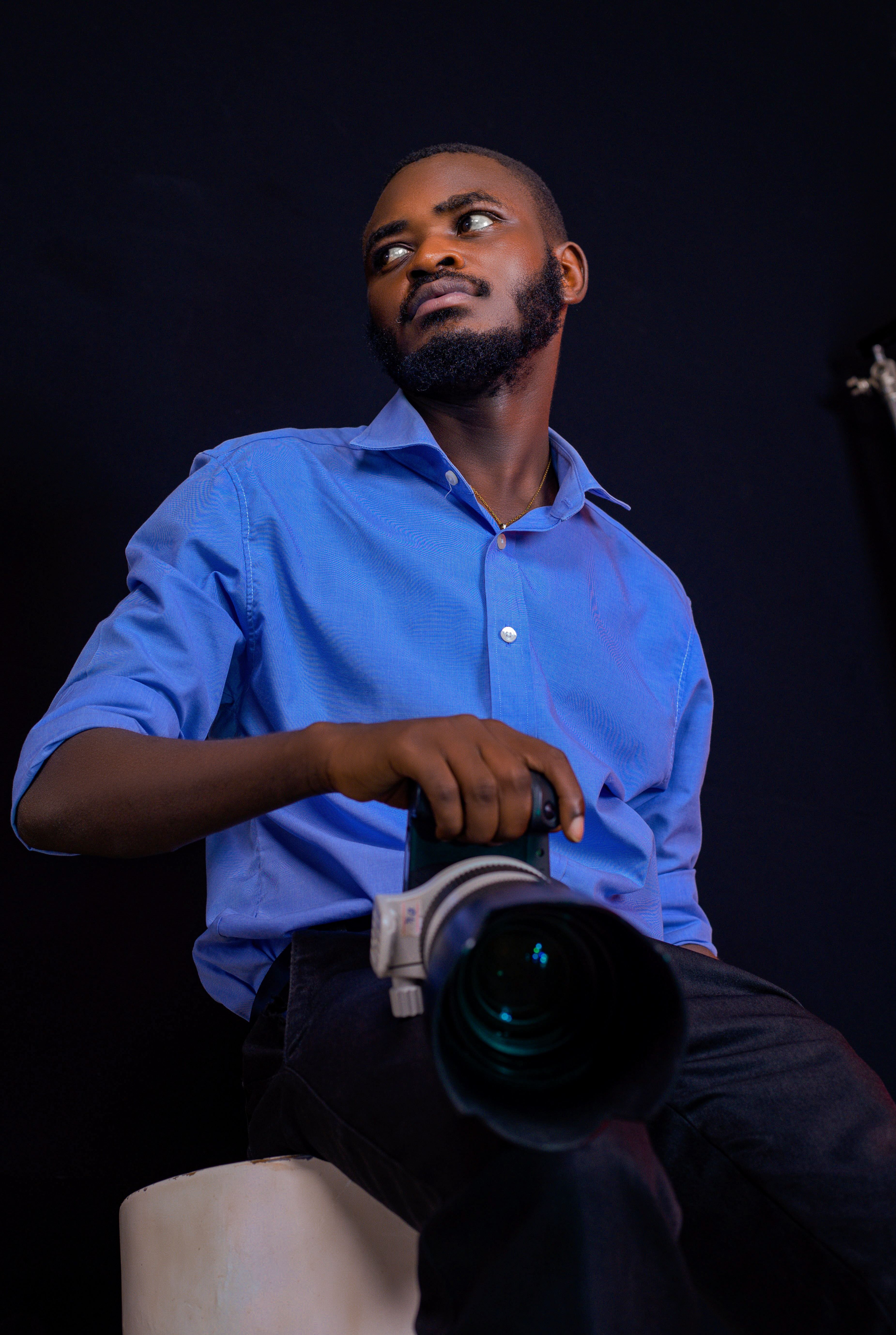 A focused photographer holding a camera in a studio with a dark backdrop.